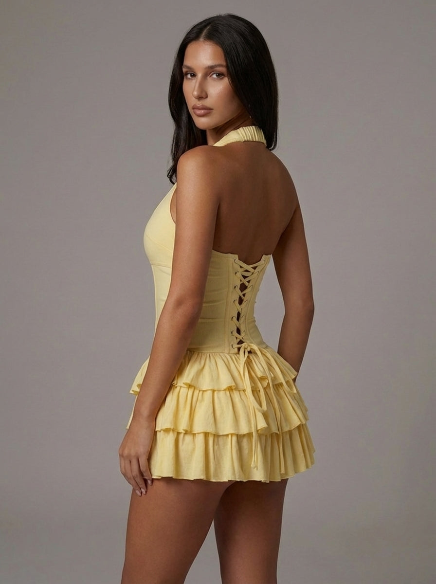 Back angle of yellow halter mini dress with lace-up corset back detail and layered ruffle skirt