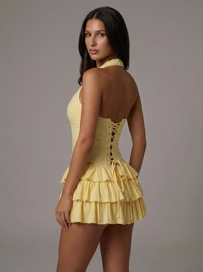 Back angle of yellow halter mini dress with lace-up corset back detail and layered ruffle skirt