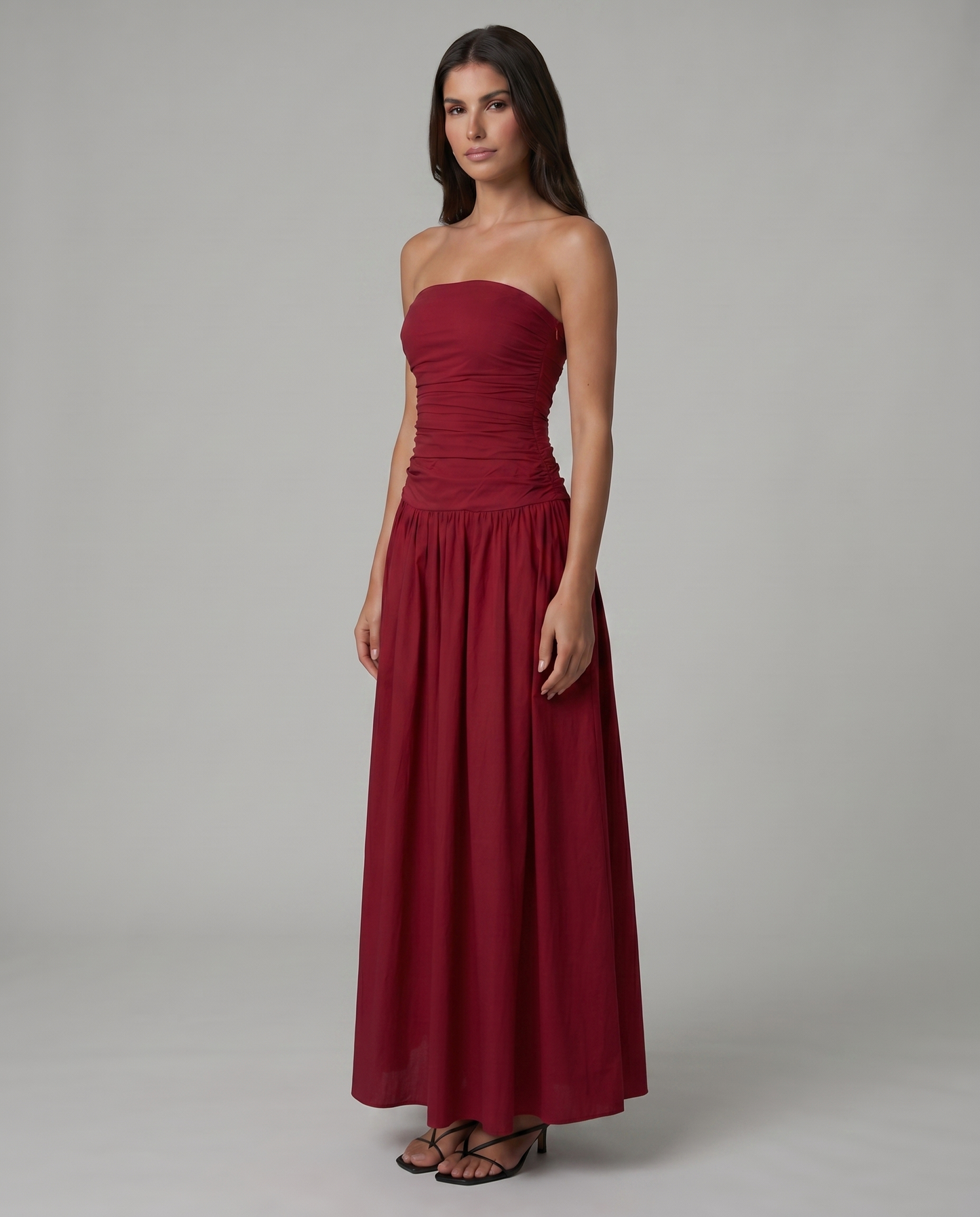 Three-quarter view of red strapless maxi dress with ruched waist and flowy skirt