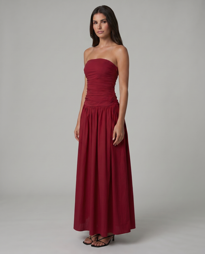 Three-quarter view of red strapless maxi dress with ruched waist and flowy skirt