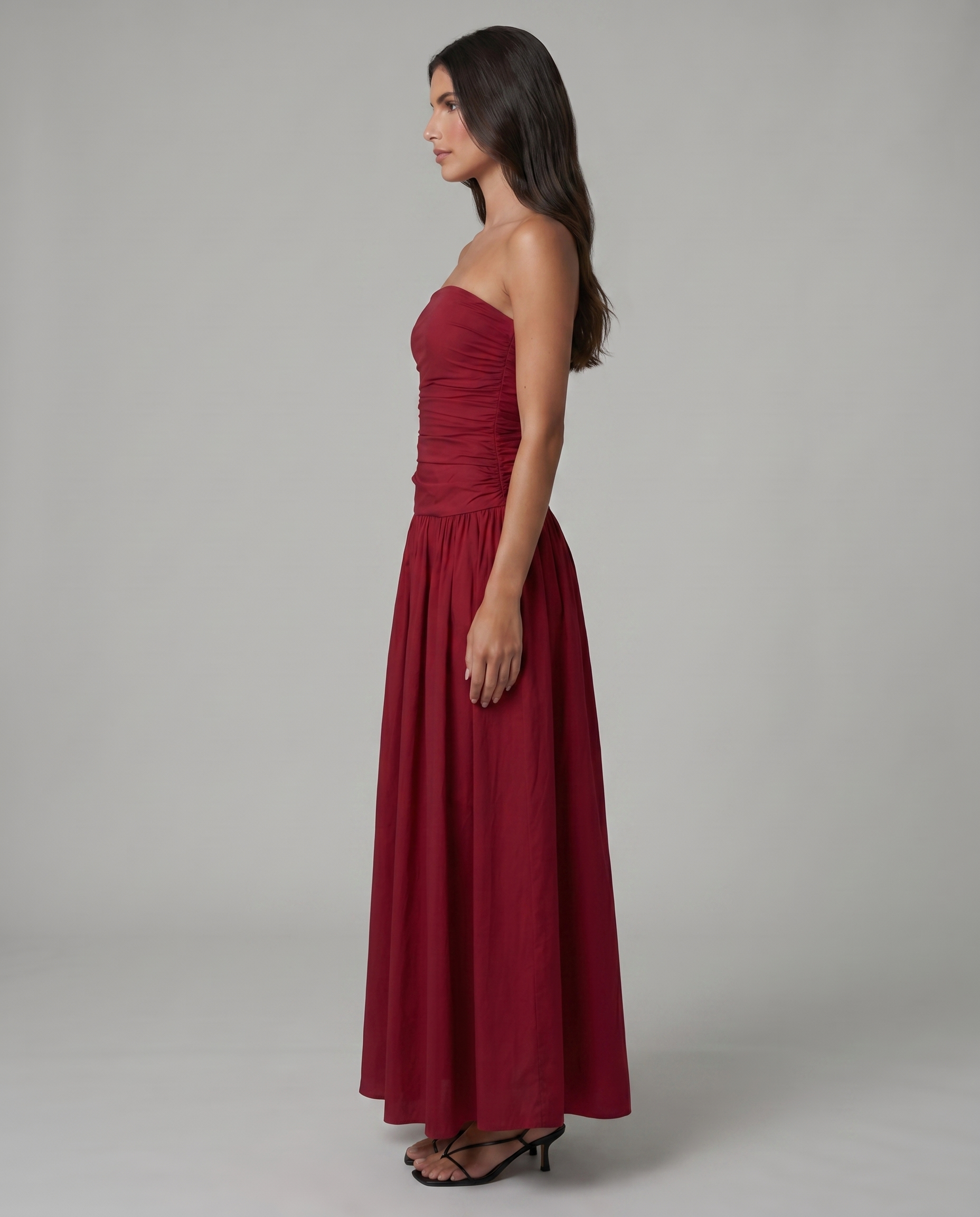 Side profile of red strapless maxi dress with fitted ruched bodice and ankle-length hem