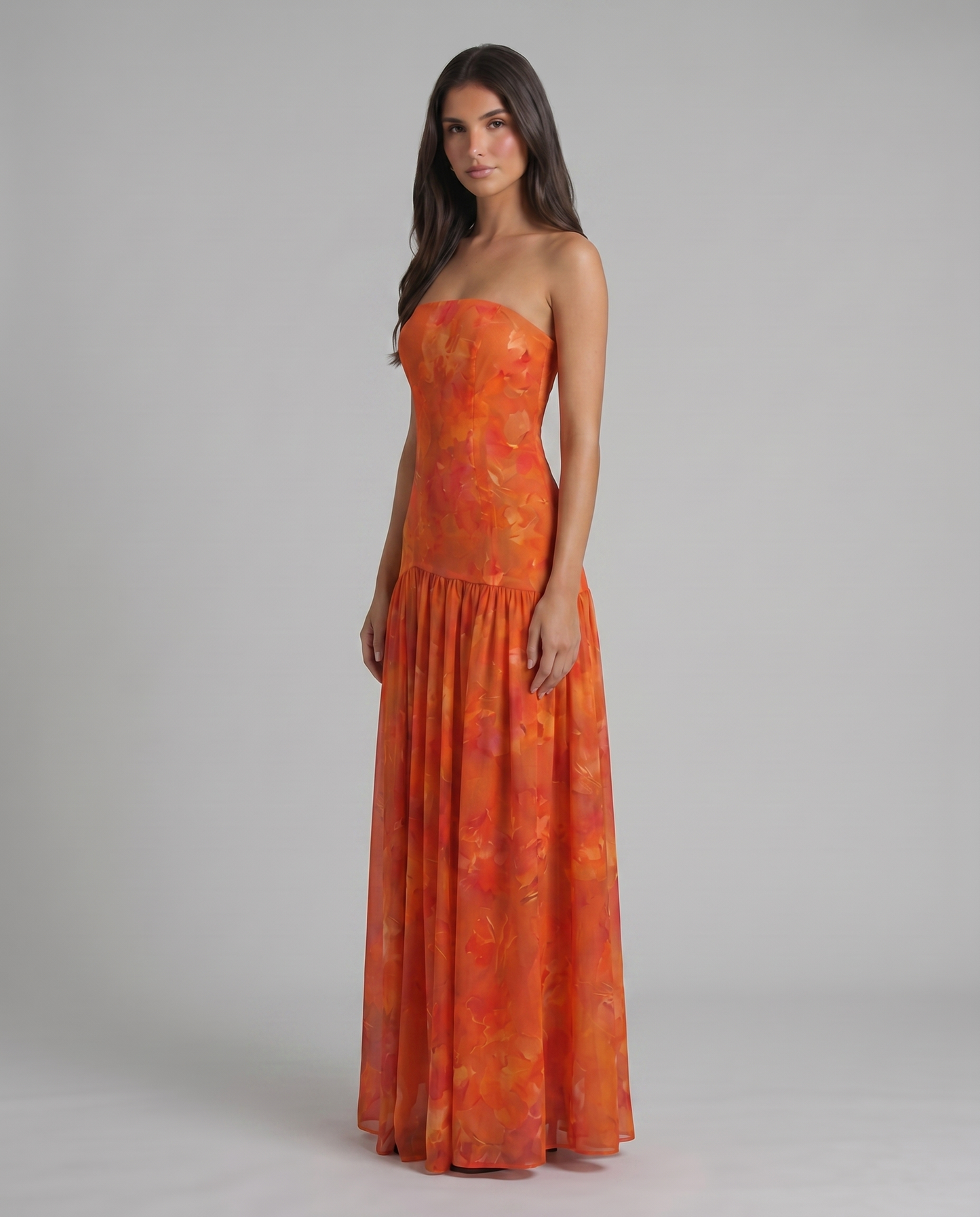 Three-quarter view of red strapless maxi dress with watercolor floral print and drop-waist seam