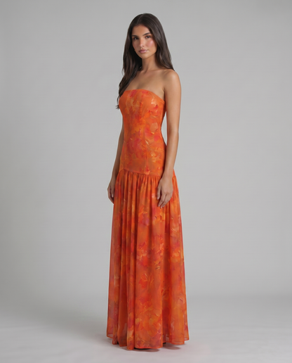 Three-quarter view of red strapless maxi dress with watercolor floral print and drop-waist seam