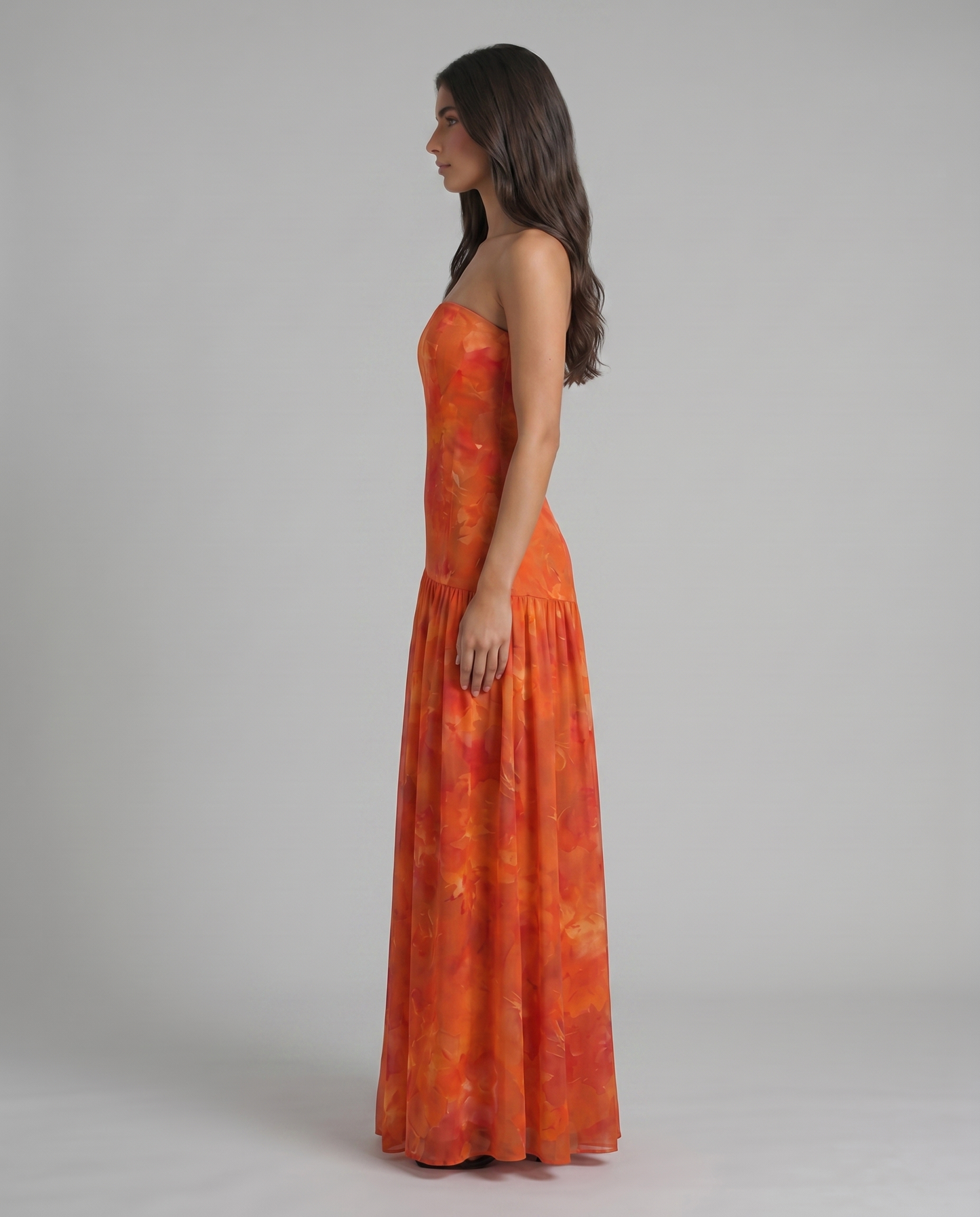 Side profile of red floral strapless maxi dress with smooth bodice and long draped skirt