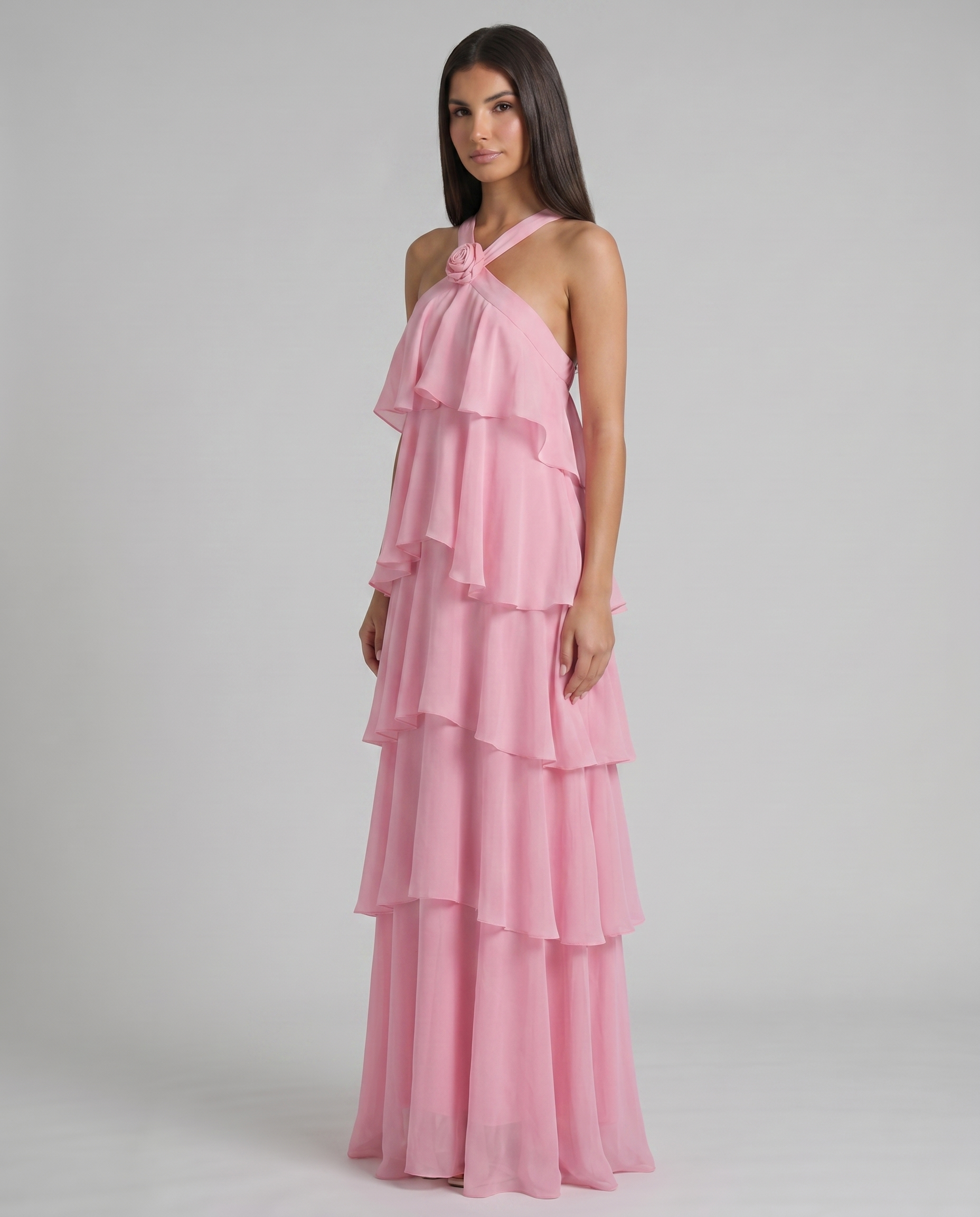 Angled view of pink ruffle maxi dress with rosette halter neckline and cascading layered chiffon tiers