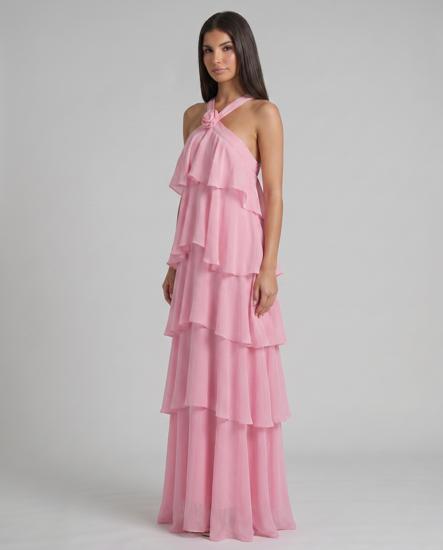 Three-quarter view of pink ruffle maxi dress with rosette halter neckline and multi-tier chiffon skirt
