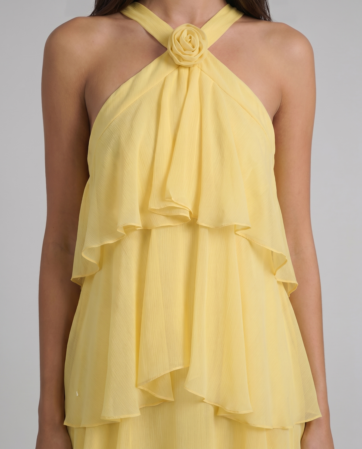 Detail shot of yellow flower ruffle maxi dress showing cross halter straps, rosette, and chiffon