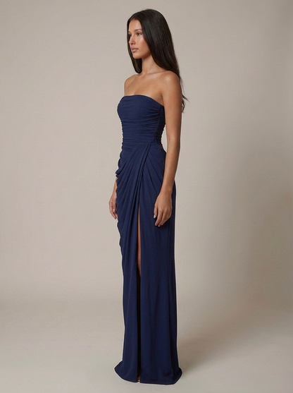 Side view navy strapless maxi dress with smooth fitted bodice, draped skirt, and front slit