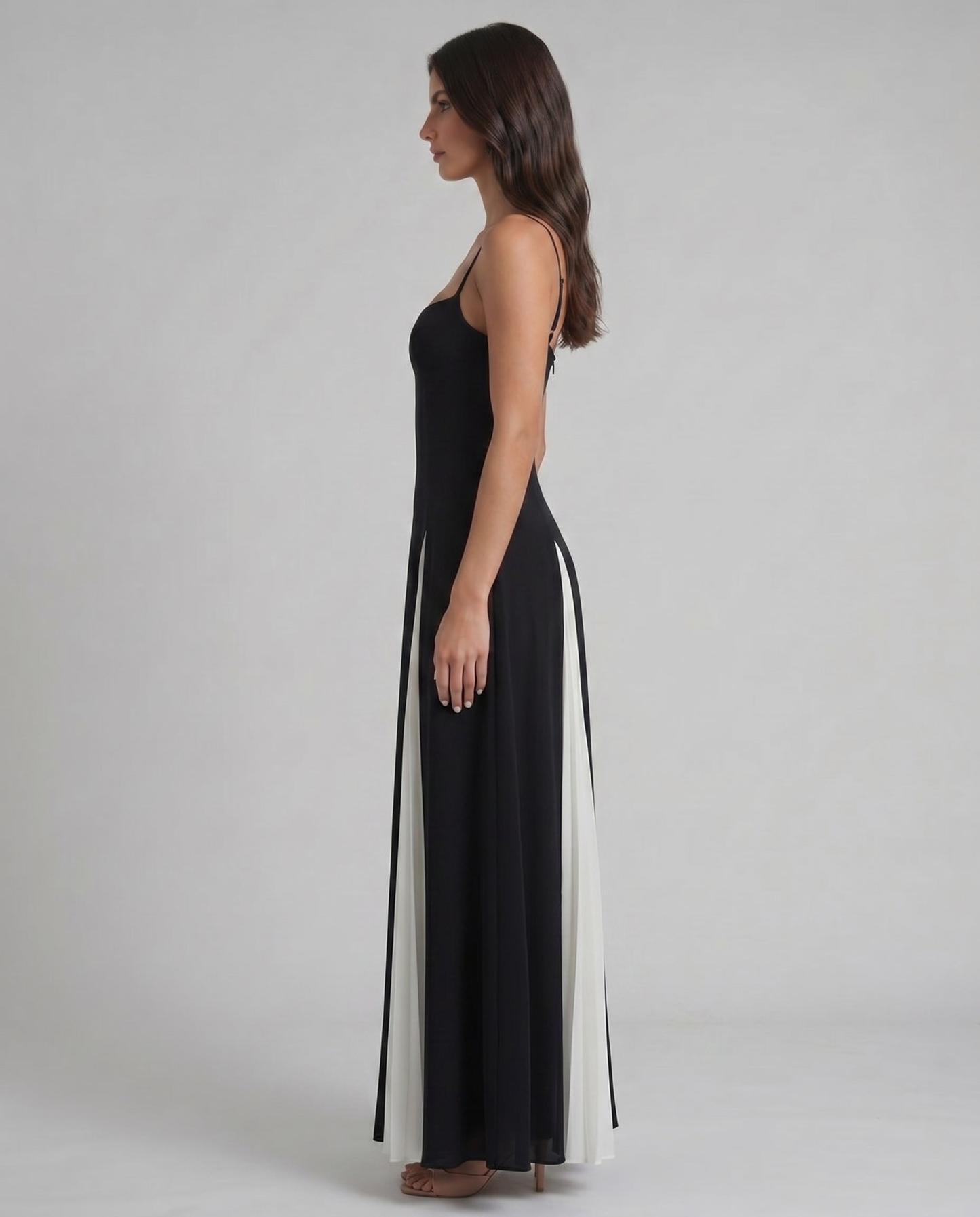 Side profile of white and black maxi dress showing slim silhouette, thin straps, and pleated skirt detail