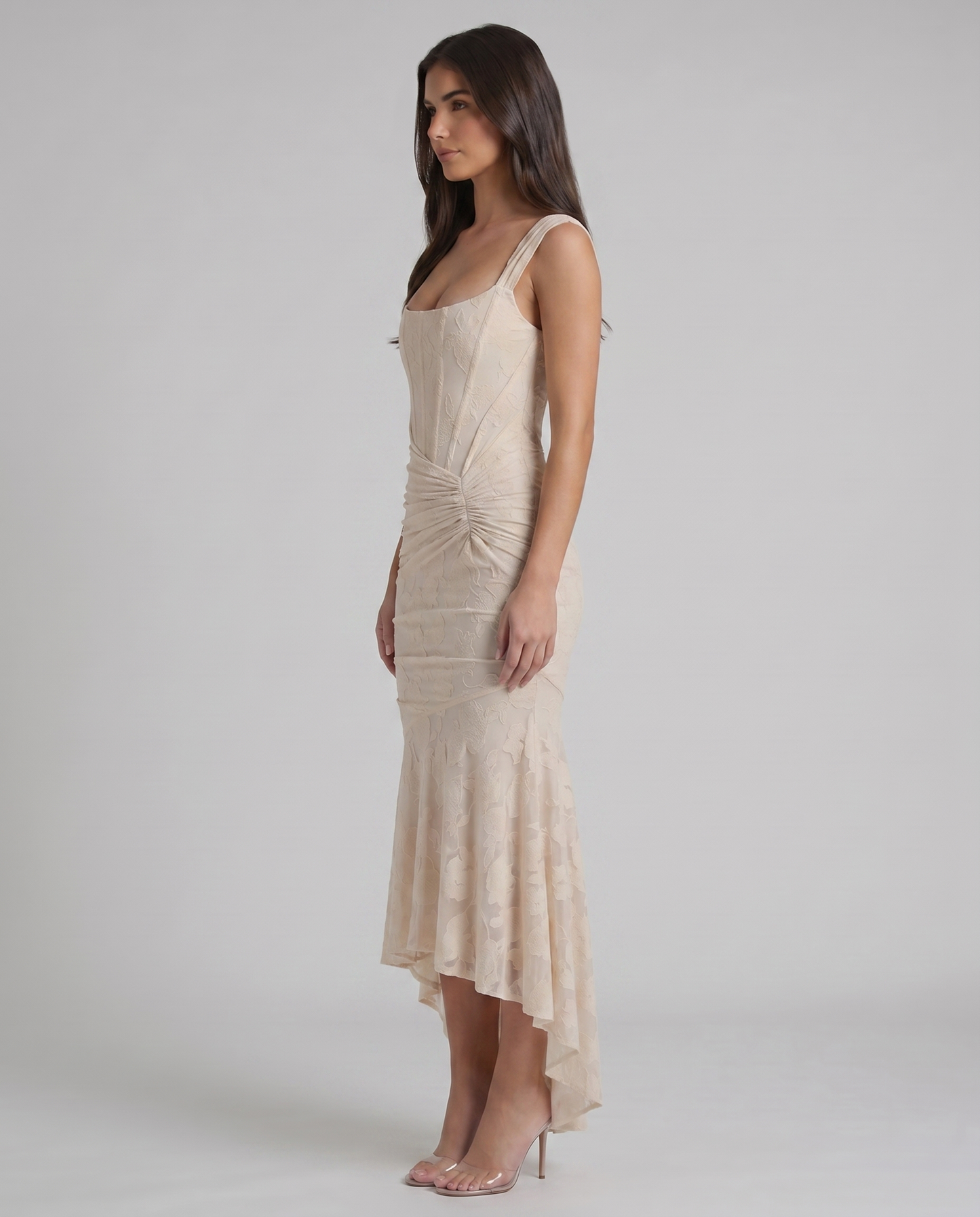 Side profile of beige lace corset maxi dress with structured bodice seams, ruched waist and high-low skirt