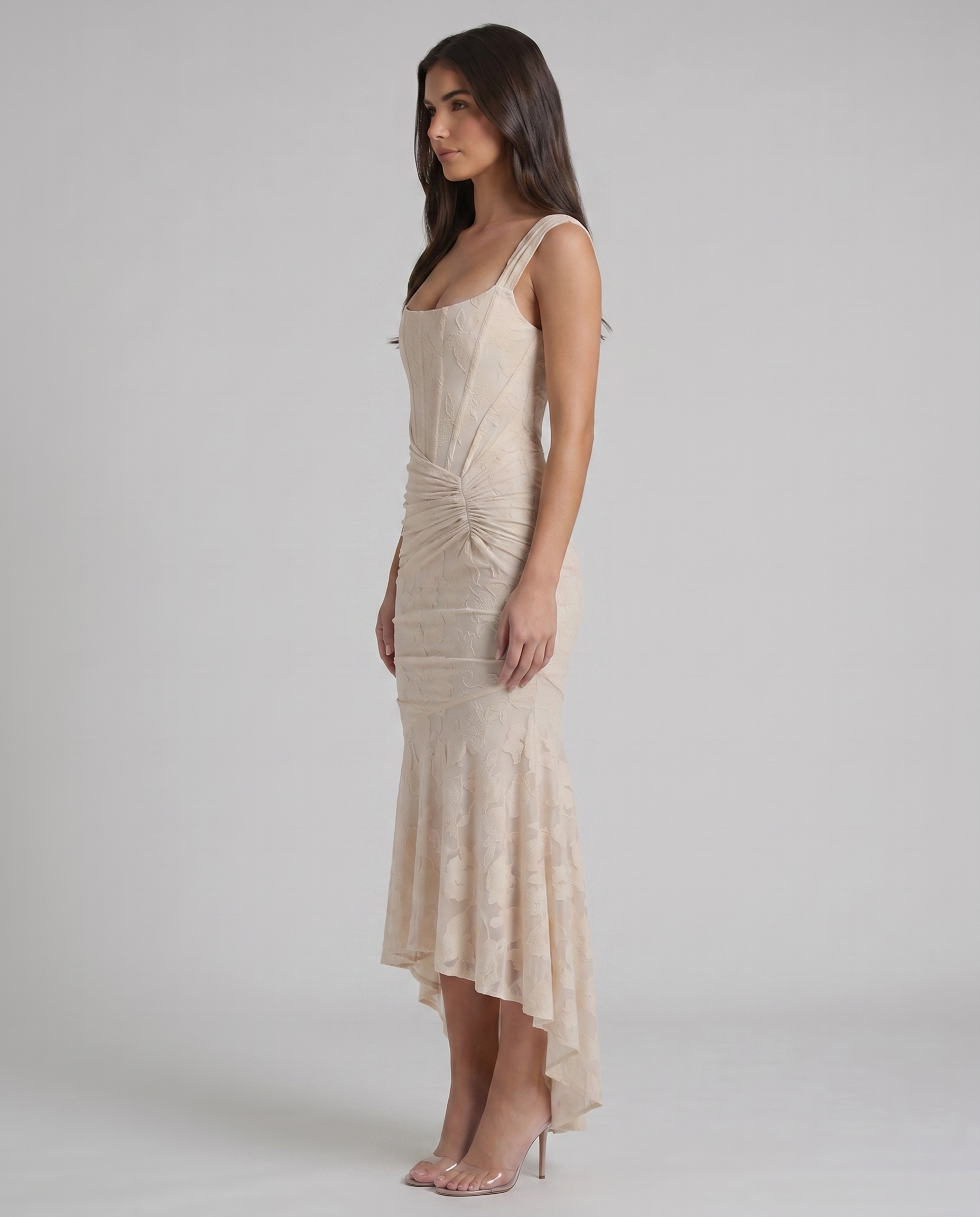 Side profile of beige lace corset maxi dress with structured bodice seams, ruched waist and high-low skirt