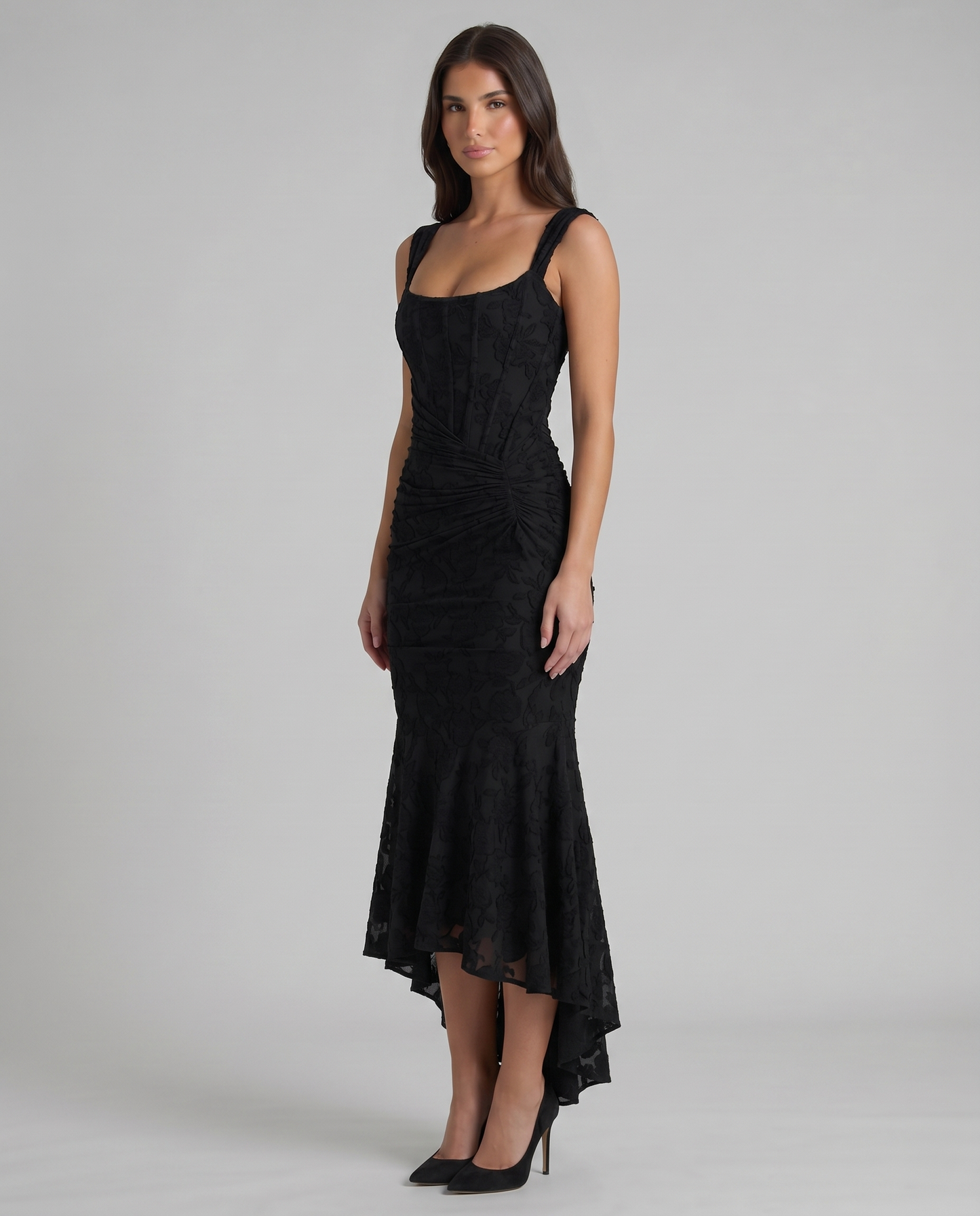 Angled view of black corset maxi dress showing fitted bodice seams, gathered waist and flared hem