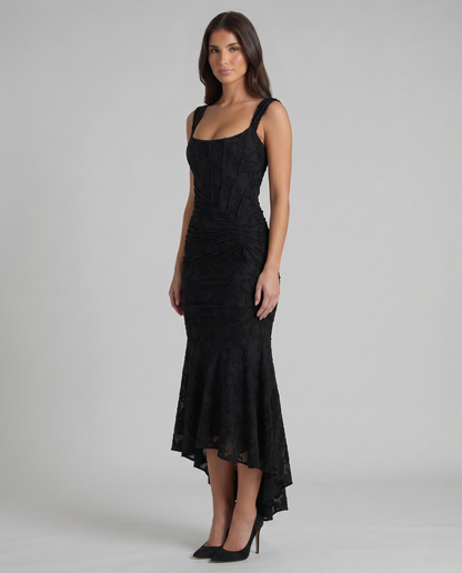 Angled view of black corset maxi dress showing fitted bodice seams, gathered waist and flared hem