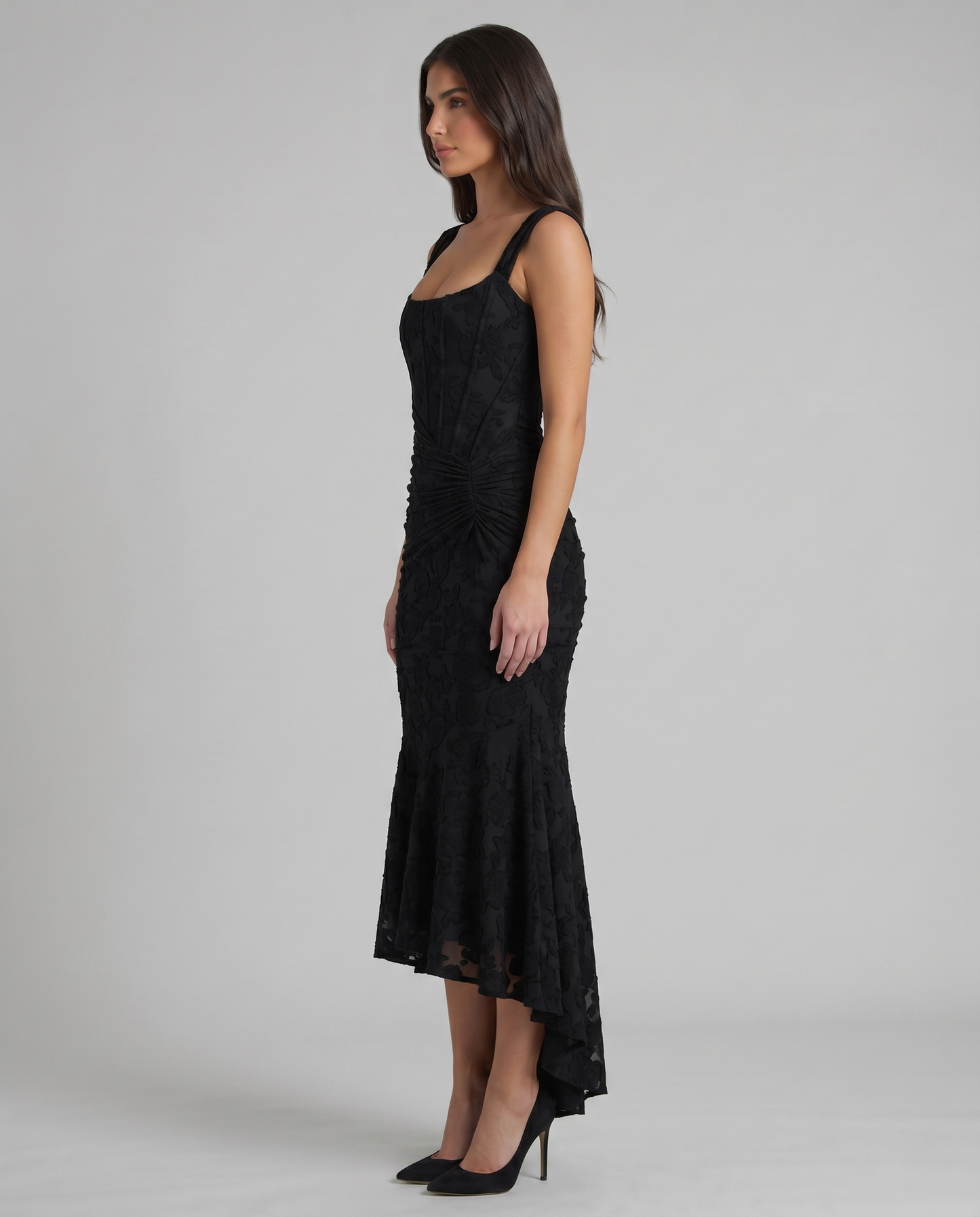 Side profile of black corset maxi dress with structured bodice, ruched hip detail and high-low skirt