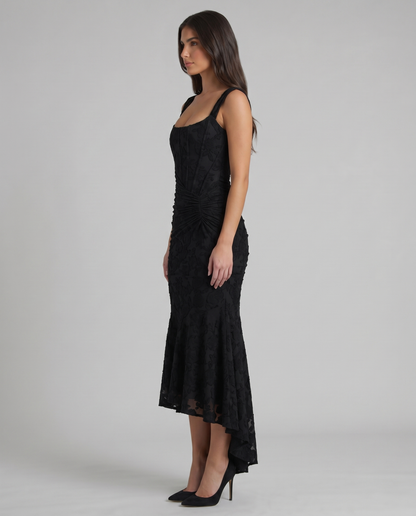 Side profile of black corset maxi dress with structured bodice, ruched hip detail and high-low skirt