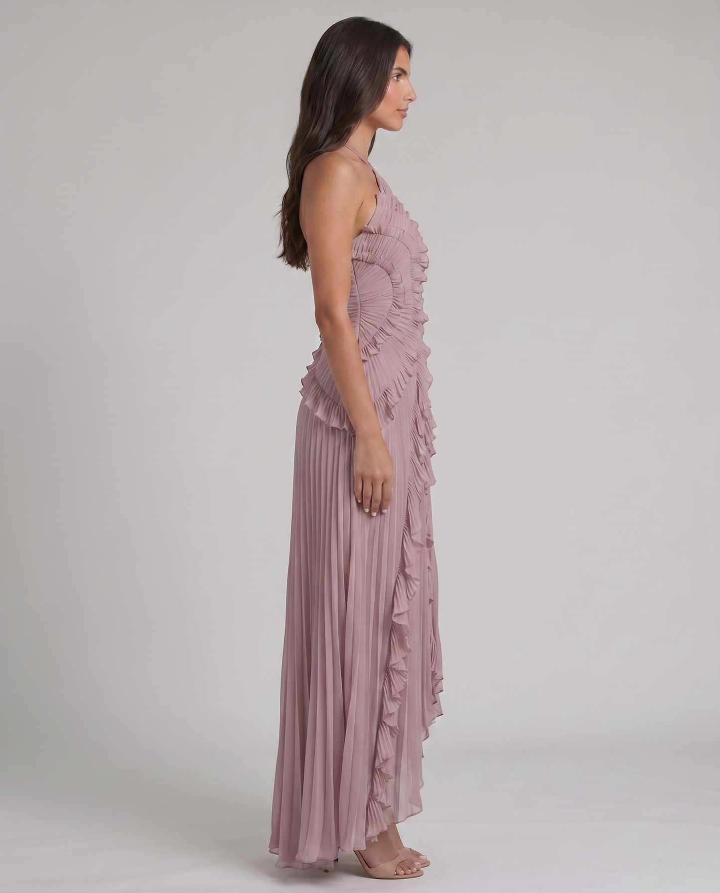 Side profile of pink pleated maxi dress with fitted ruched bodice, layered ruffles, and flowy skirt